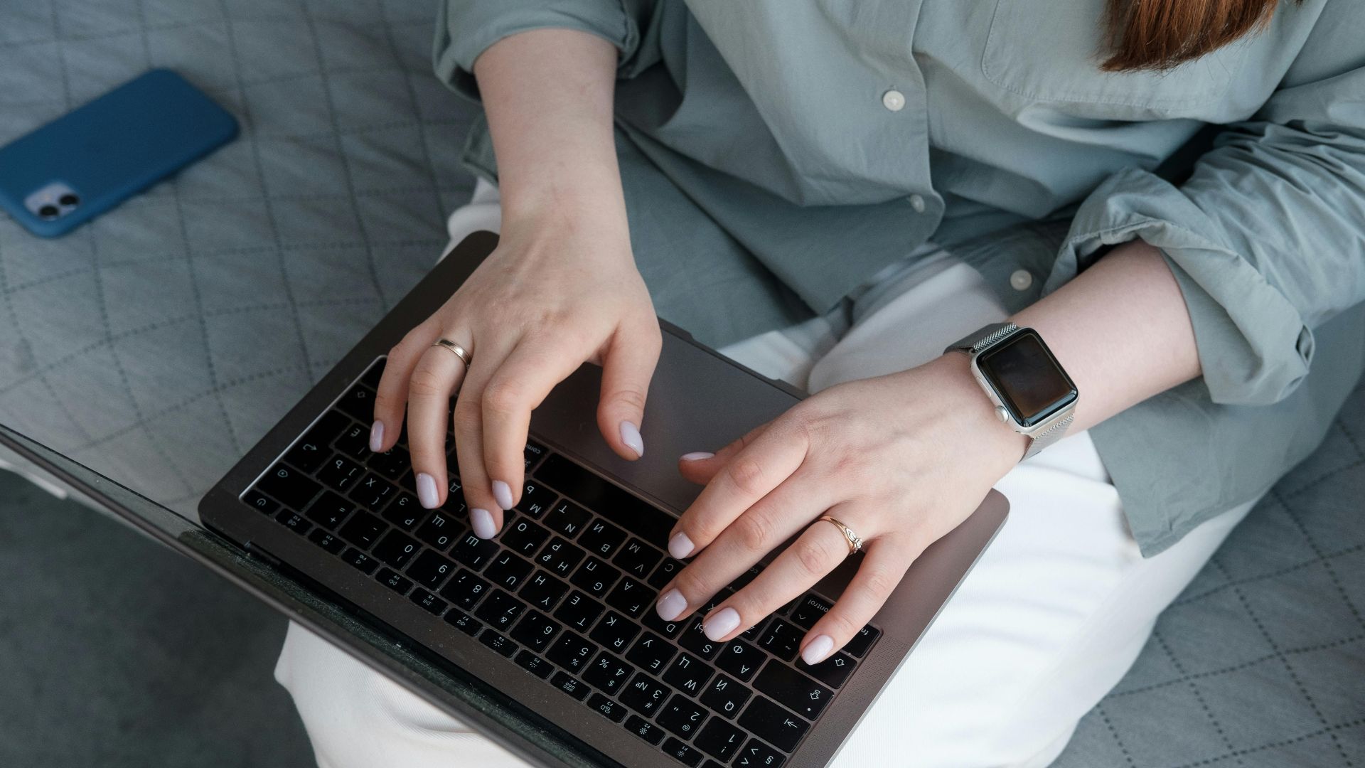 Close-up of a woman typing on a laptop while wearing a smartwatch and rings, indoors.