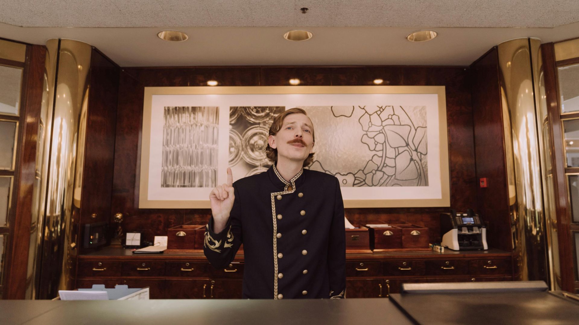 A luxury hotel receptionist in uniform stands behind the opulent front desk, ready to assist guests.