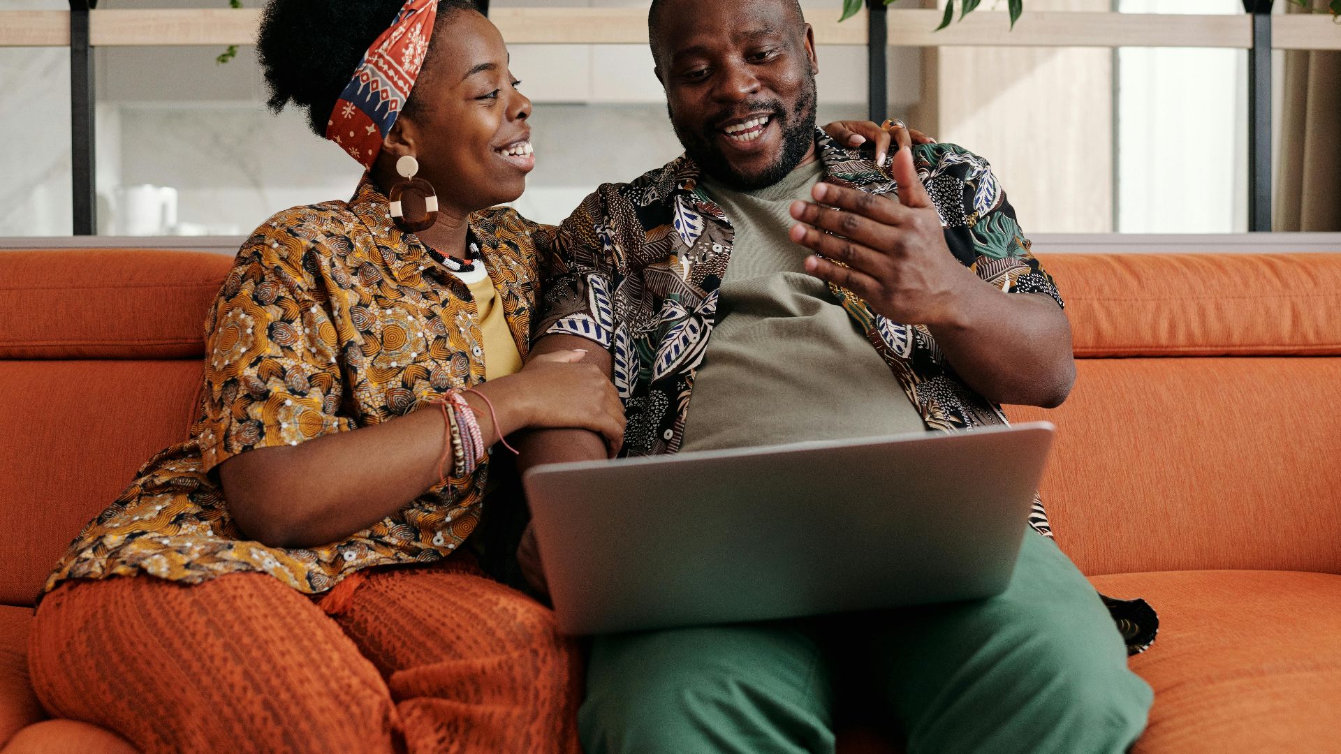 A cheerful Black couple sitting on a couch, enjoying a moment together with a laptop.