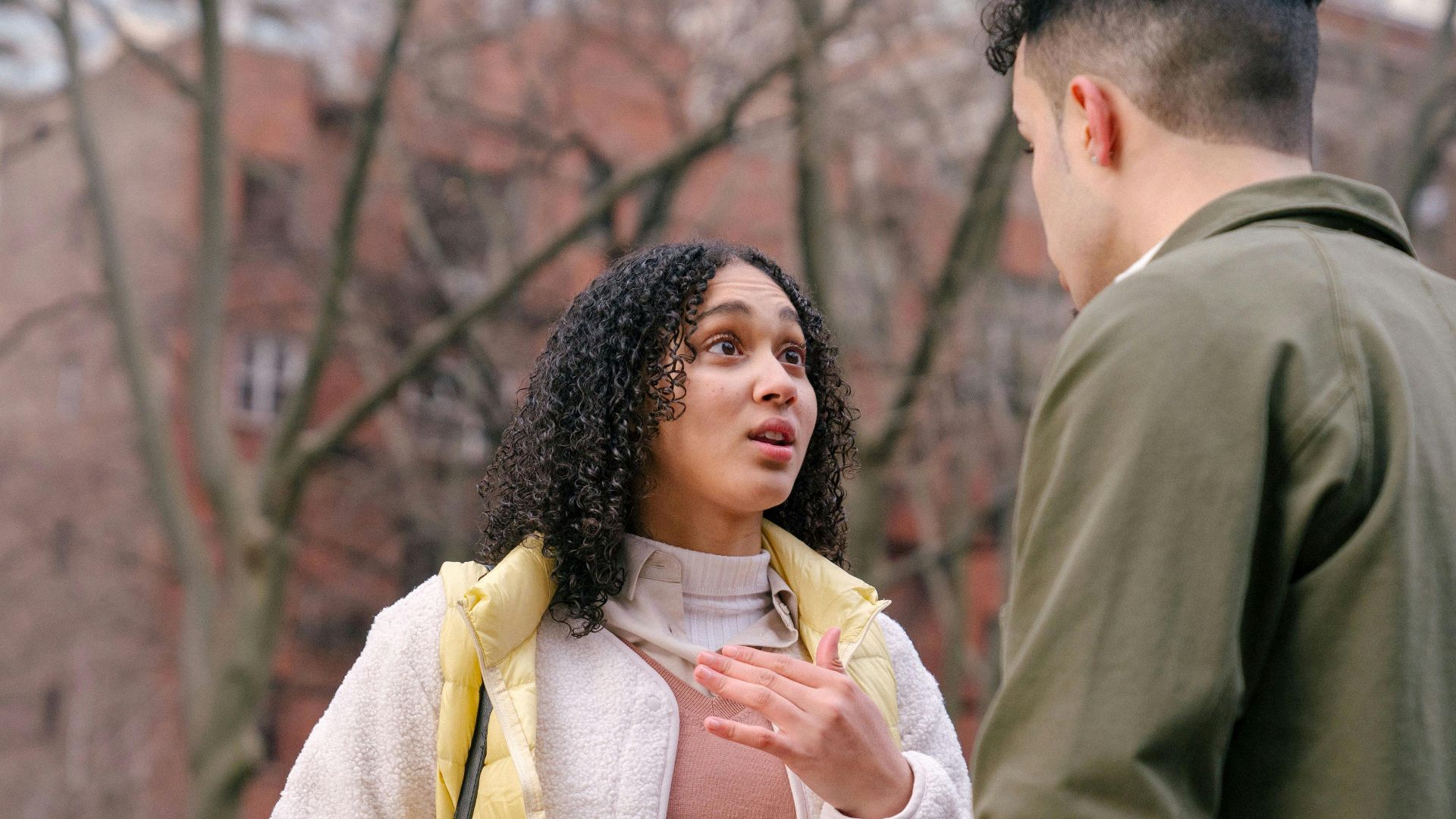 From below of ethnic female with short curly hair standing and arguing with boyfriend on street in daylight