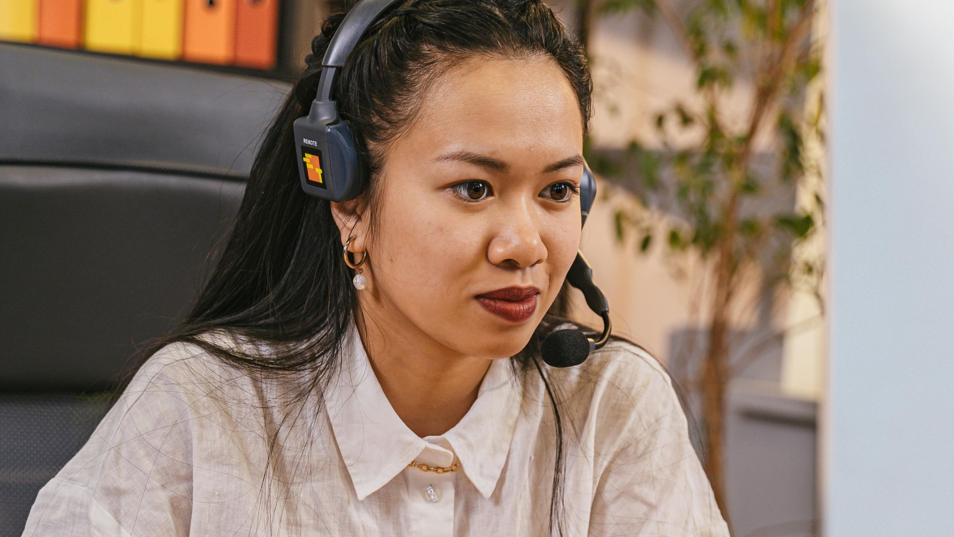 Asian woman using computer and headset in a modern office setting.