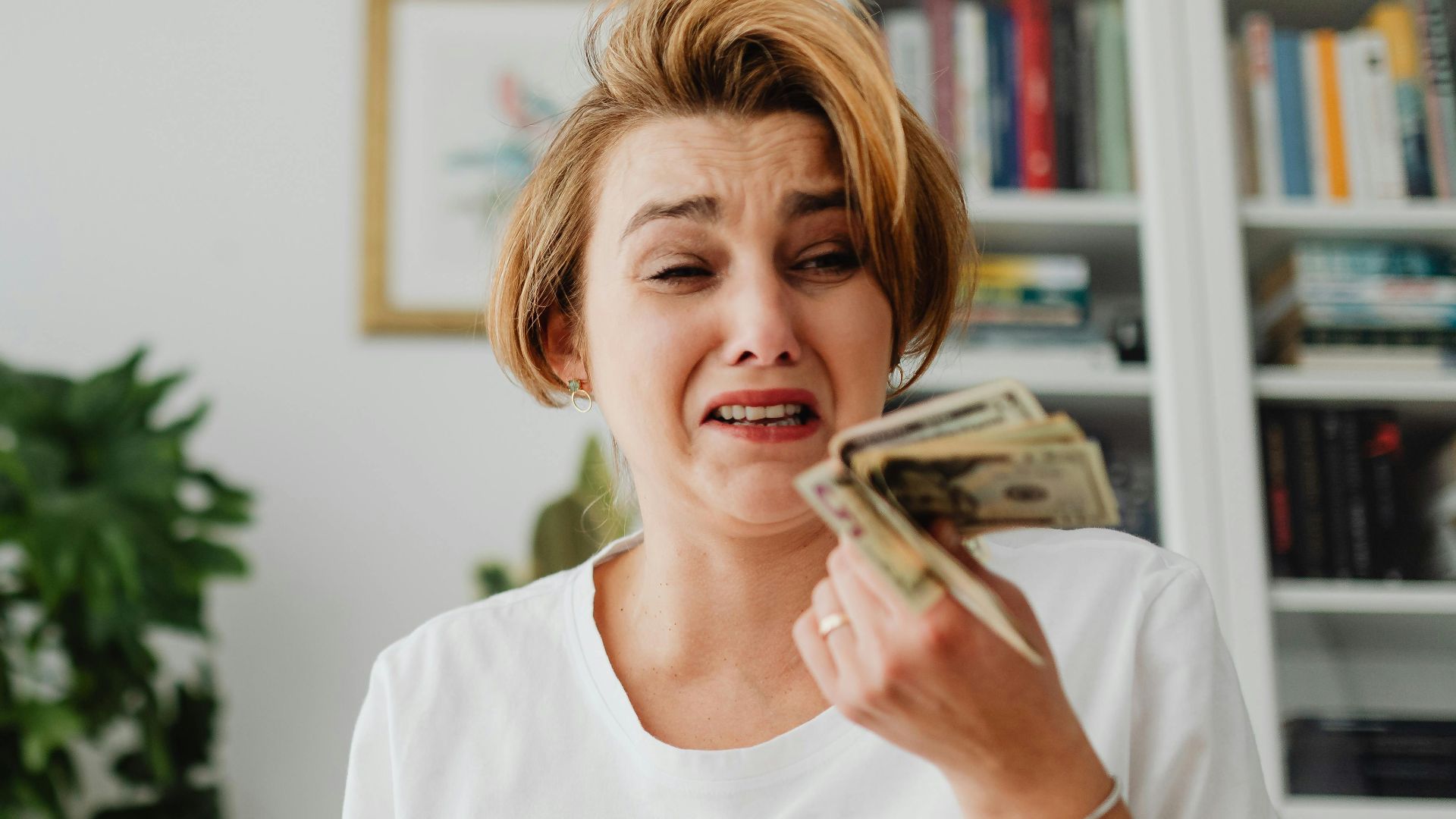 A woman looking stressed while counting money in a living room setting.