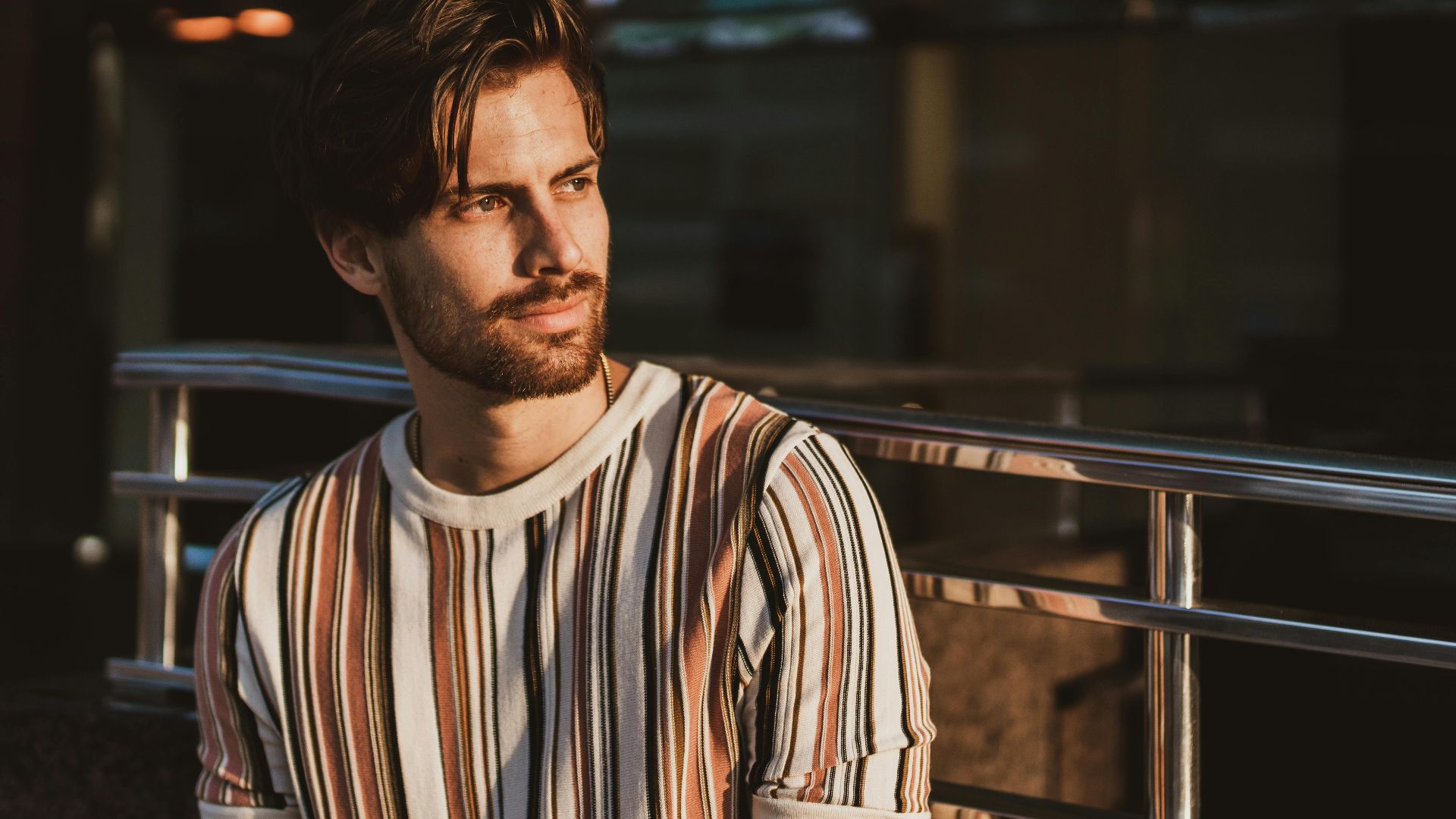 A thoughtful man in a striped shirt bathed in warm sunset light, creating a moody portrait.
