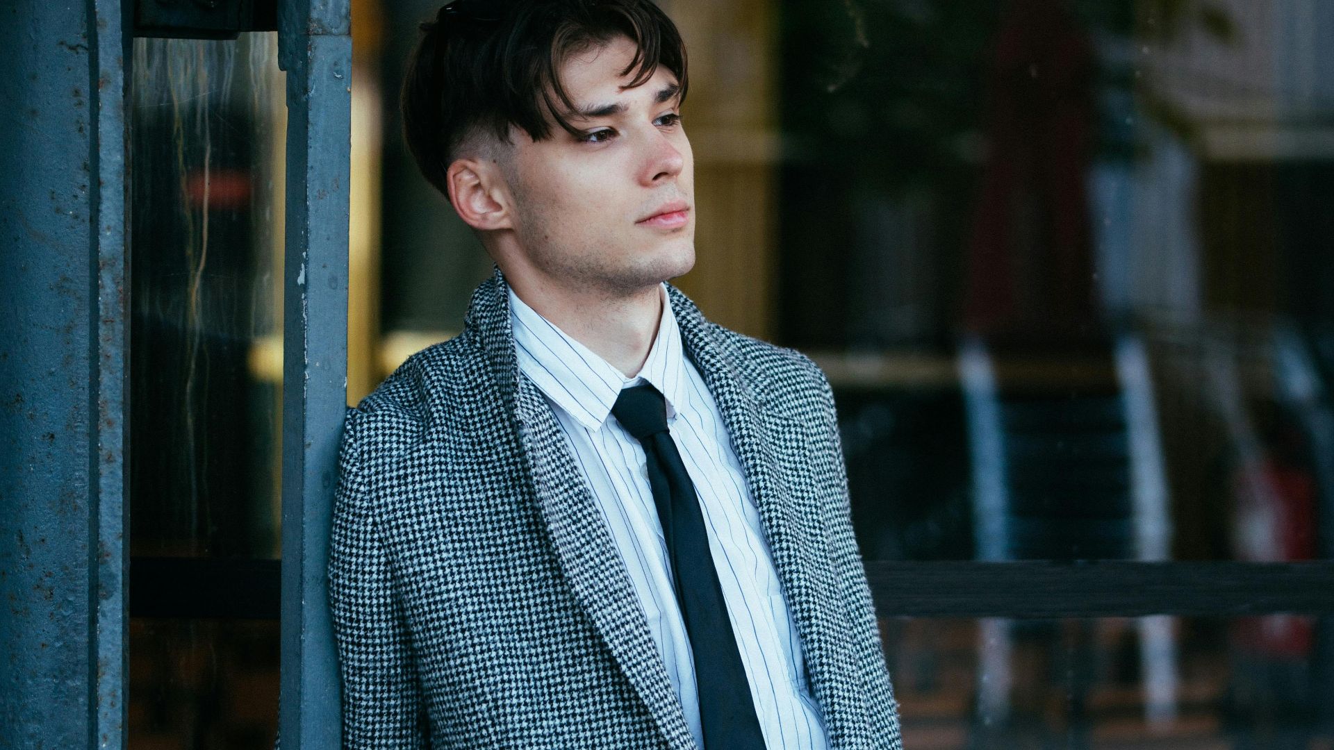 Young man in a blazer and tie leaning outdoors, exuding a confident and stylish look.