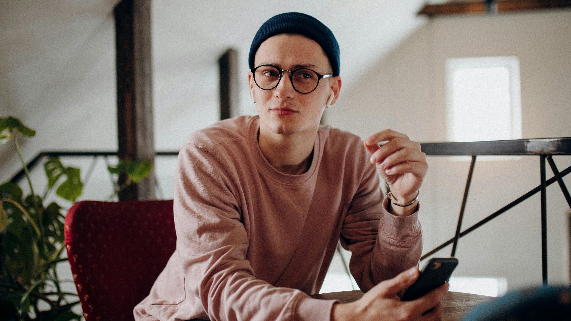Casual young man in beanie and glasses using smartphone indoors.