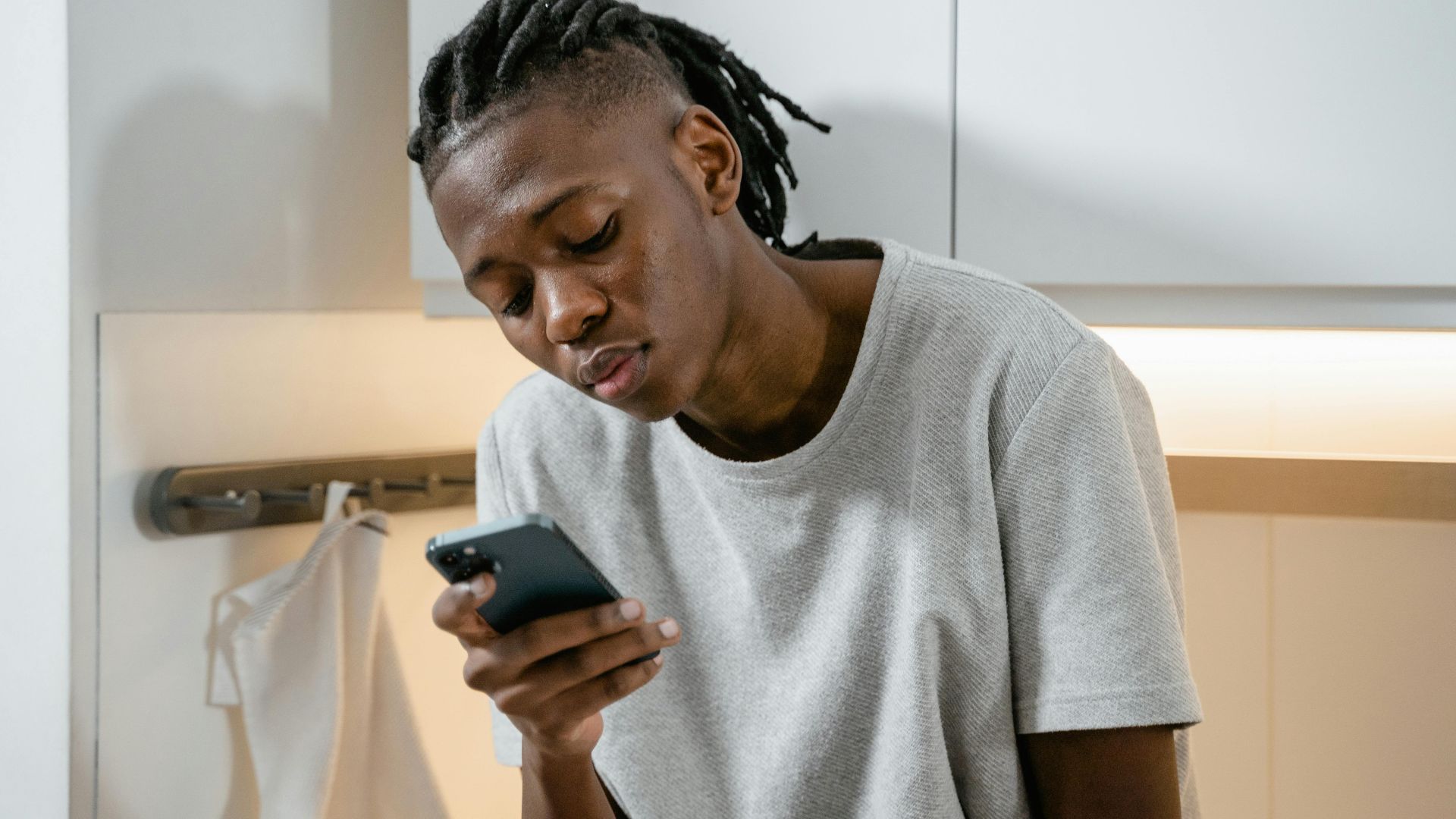 Focused individual texting on smartphone in modern kitchen environment.