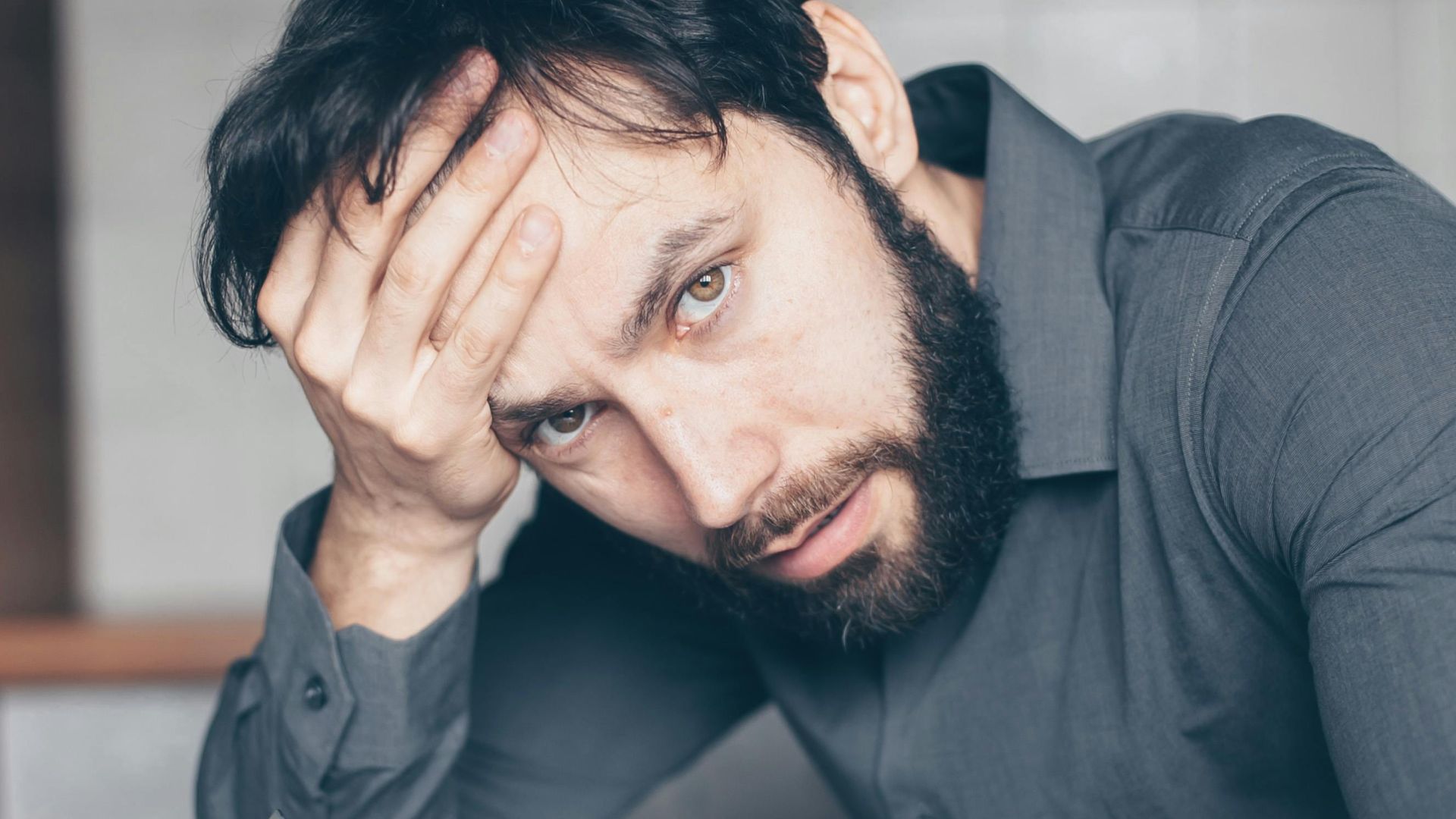 Thoughtful man sitting at a table with glasses and cup, showing frustration.