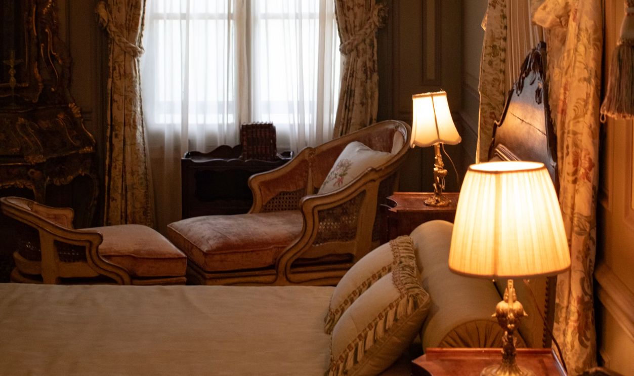 A bedroom with a bed, chair, lamps and a window