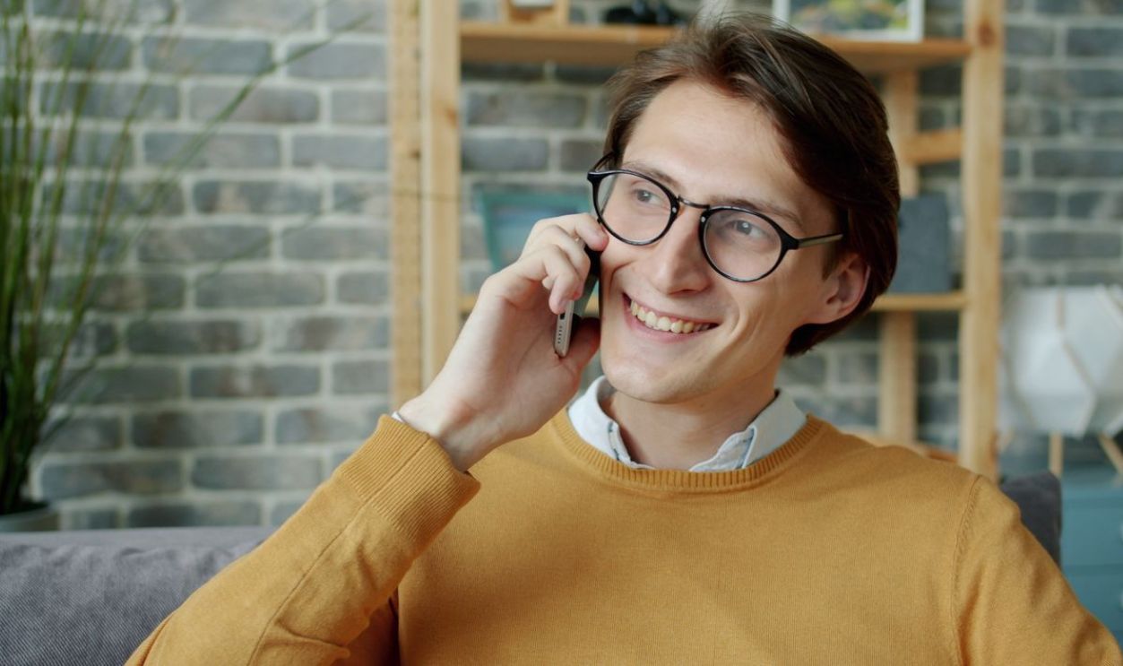 Casually dressed man enjoying a phone call indoors with a smile