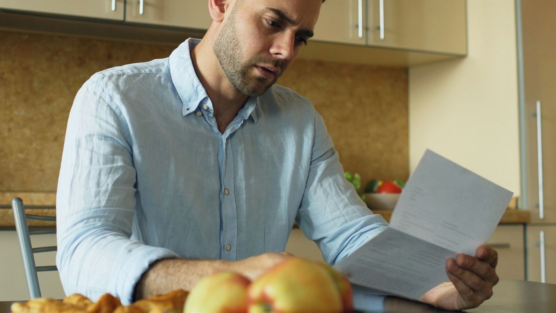 Man reading document at kitchen table with fruit and fruit