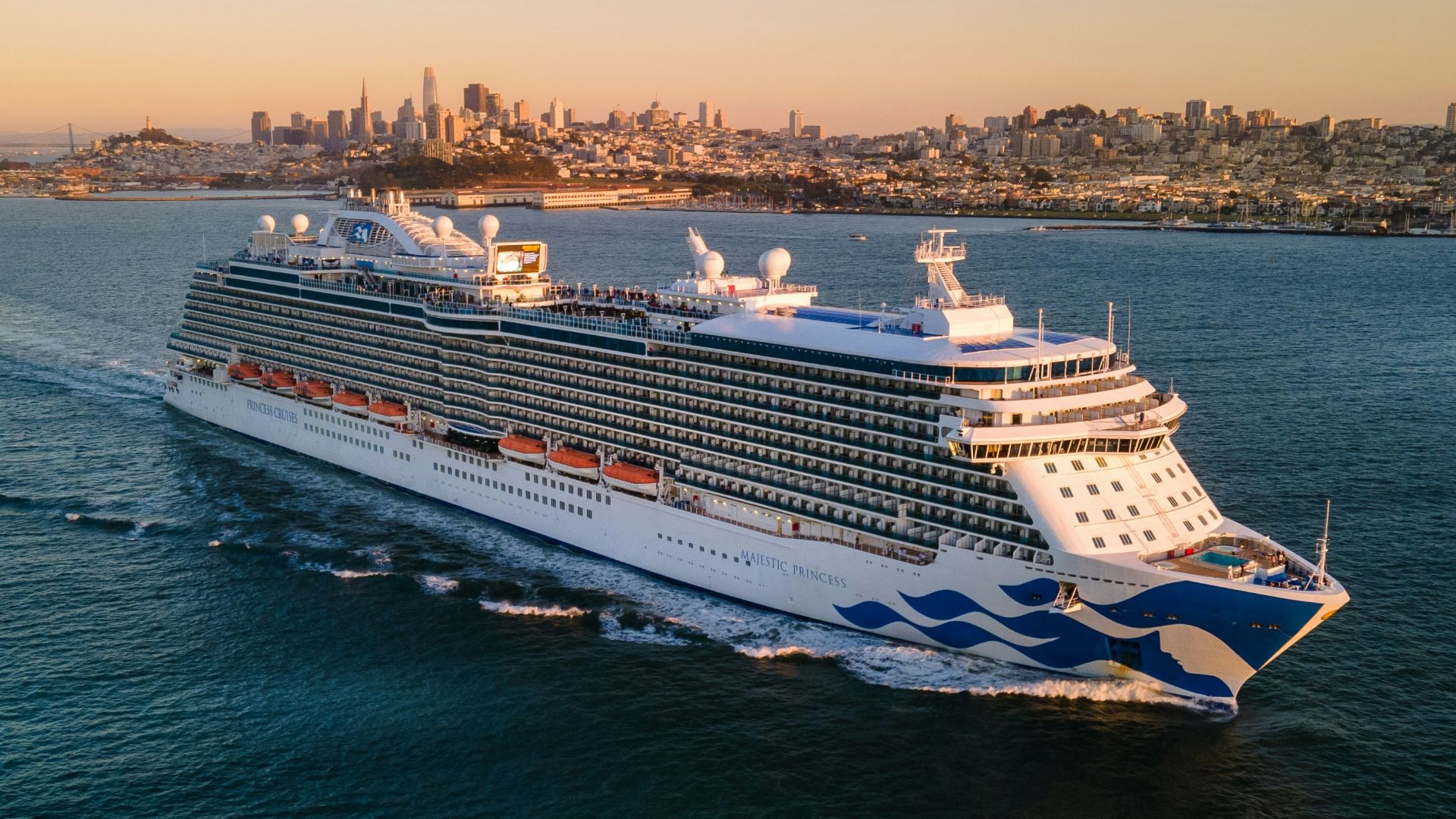 a large cruise ship in the ocean with a city in the background