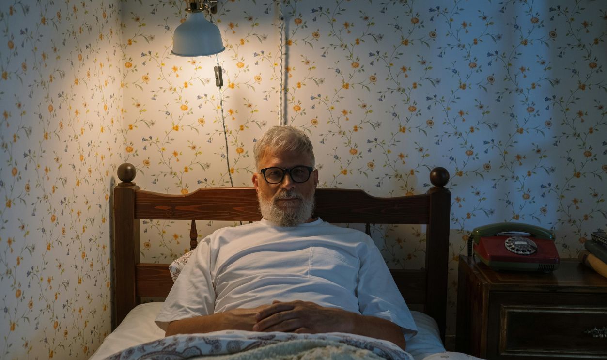 Senior man with glasses enjoying a peaceful evening in bed with warm lighting and vintage decor