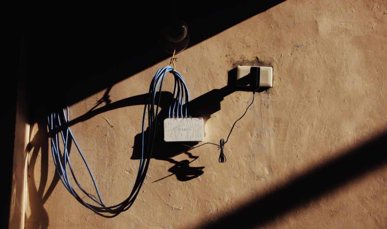 A wall outlet with blue ethernet cables and shadows creating a pattern