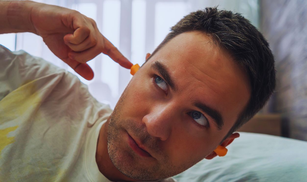 Attractive man in his 30s putting on earplugs before sleeping again because of a noisy morning and neighbors. plug in the ears for silence during sleep. noisy neighbors interfere with sleep