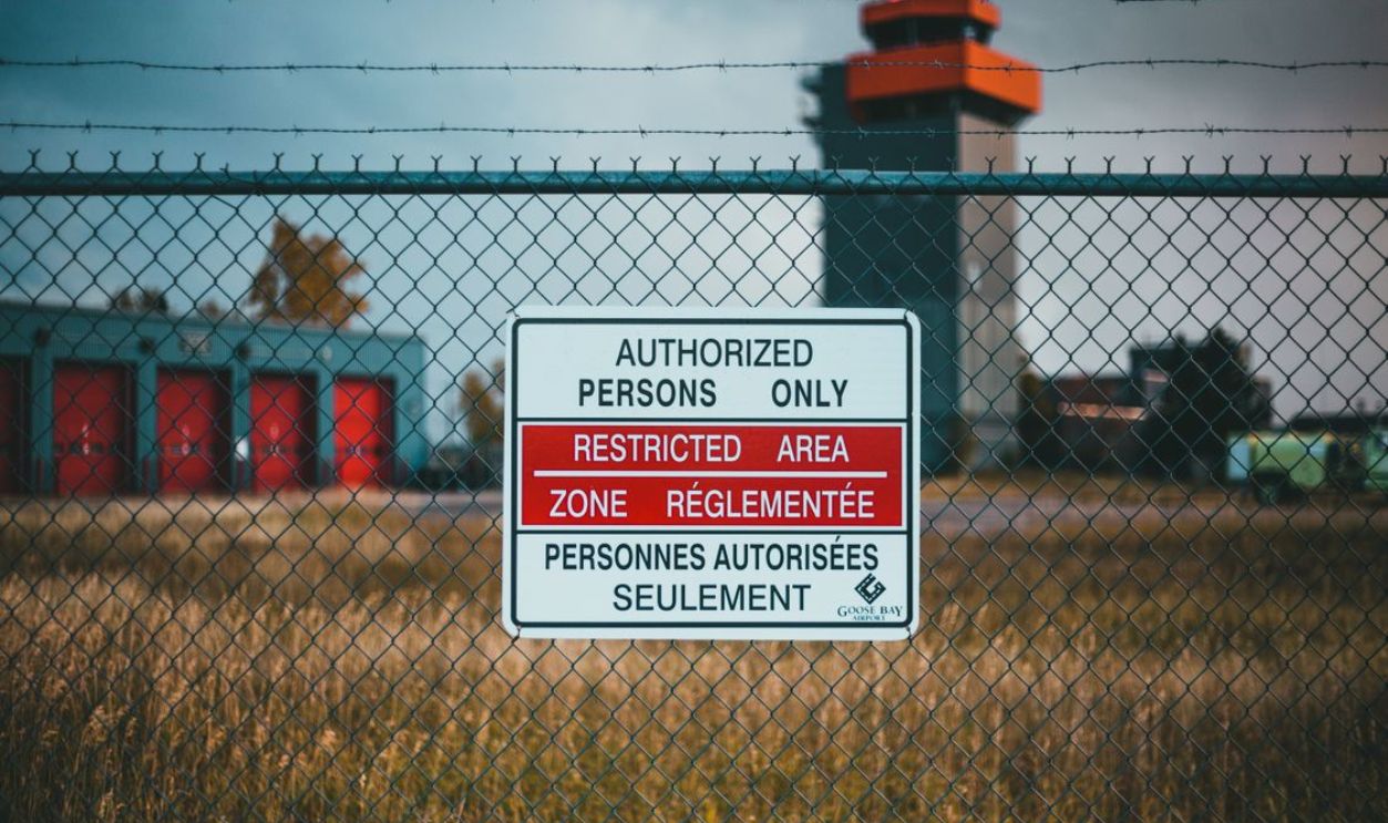 A close-up of a restricted area sign on a barbed wire fence outside an industrial area.