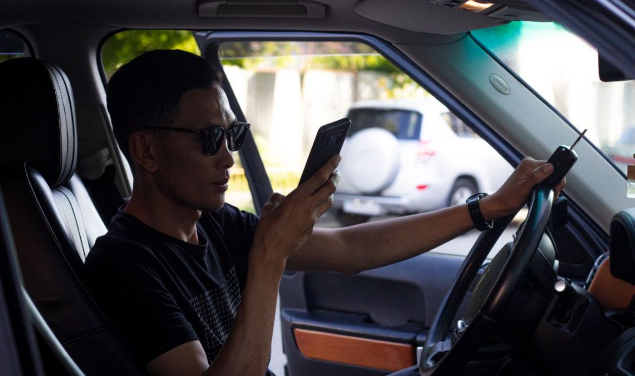 Man wearing sunglasses using a smartphone while sitting in a car. Modern car interior and technology use.