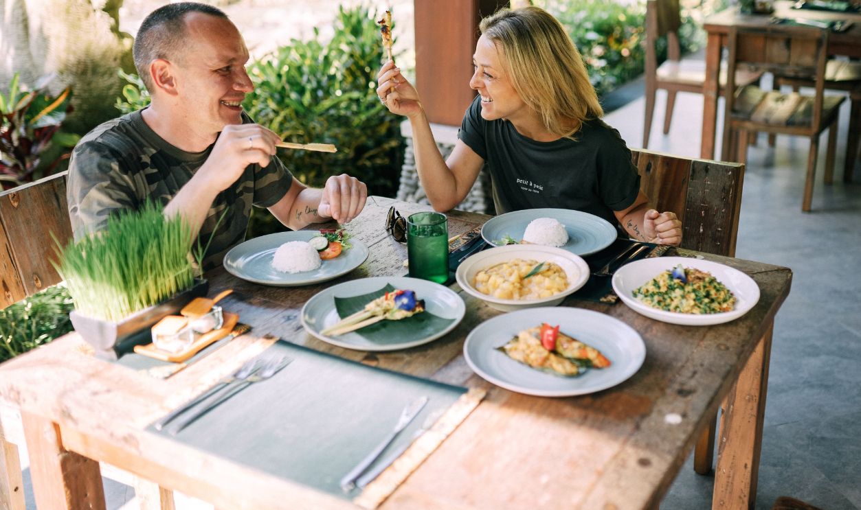 A happy couple enjoys a diverse meal at an outdoor restaurant, smiling and relaxed.