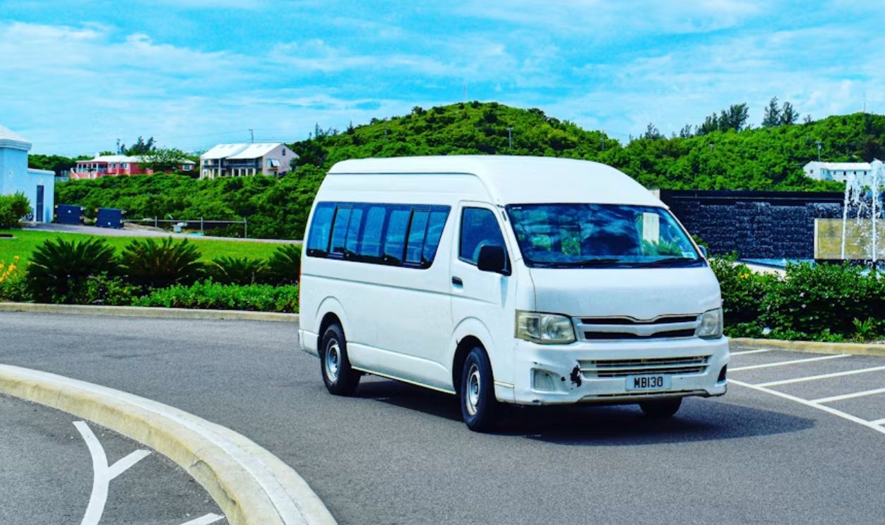 a white van driving down a street next to a lush green hillside