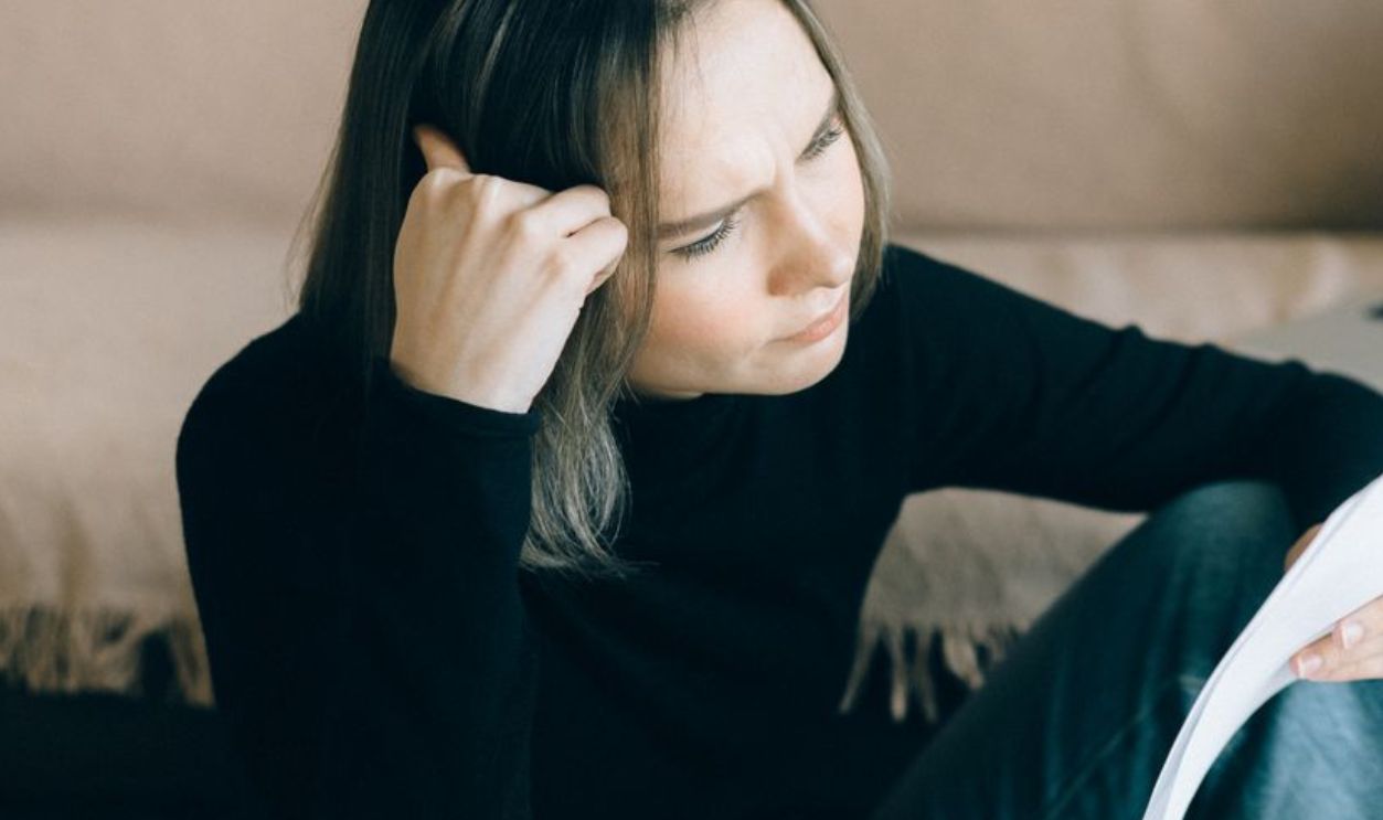 Focused woman analyzing papers with a laptop open, symbolizing thoughtful consideration