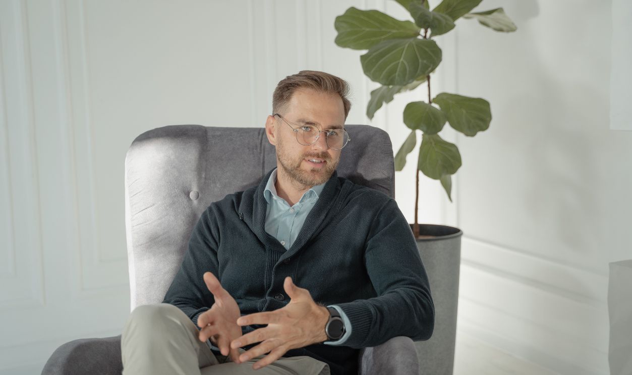 A professional man sits in an armchair talking, set indoors with a modern, bright aesthetic