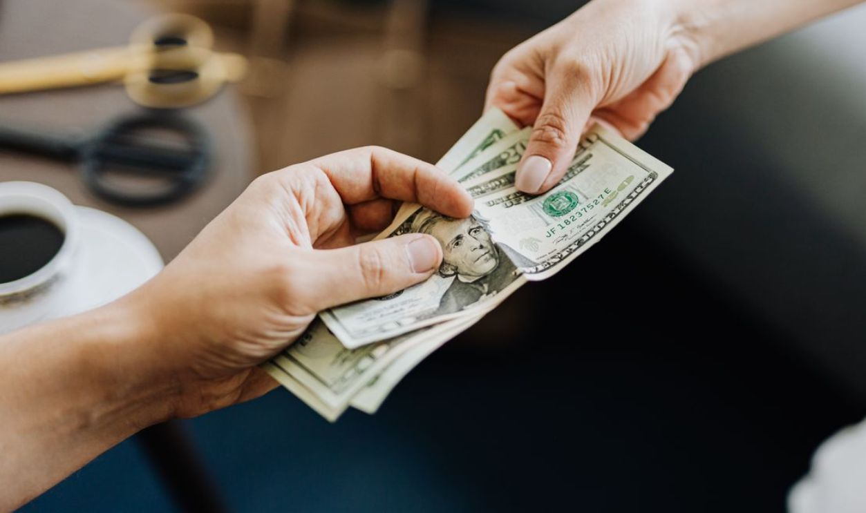 A close-up image of hands exchanging US dollar bills, symbolizing financial transaction or payment