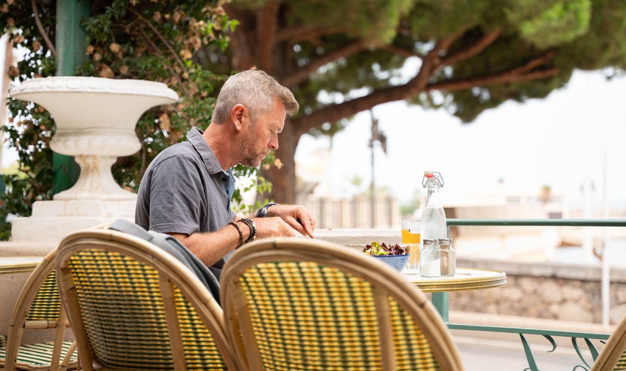 Man enjoying a relaxed meal at a beachside restaurant in Toulon, France, under sunny summer skies.