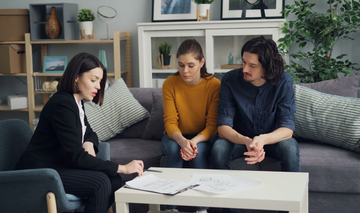 Couple discussing property with real estate agent in cozy living room setting, reviewing documents.
