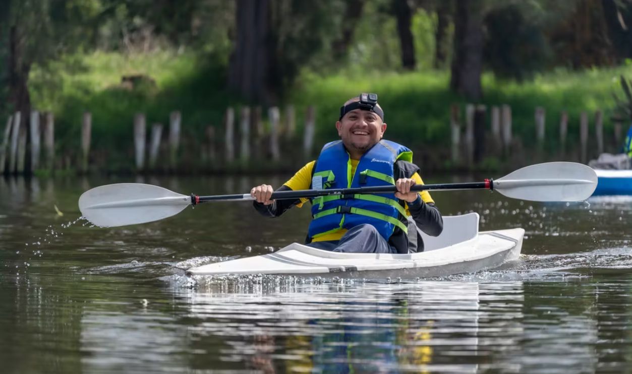 Smiling man kayaking with a paddle and life jacket in Xochimilco, Mexico