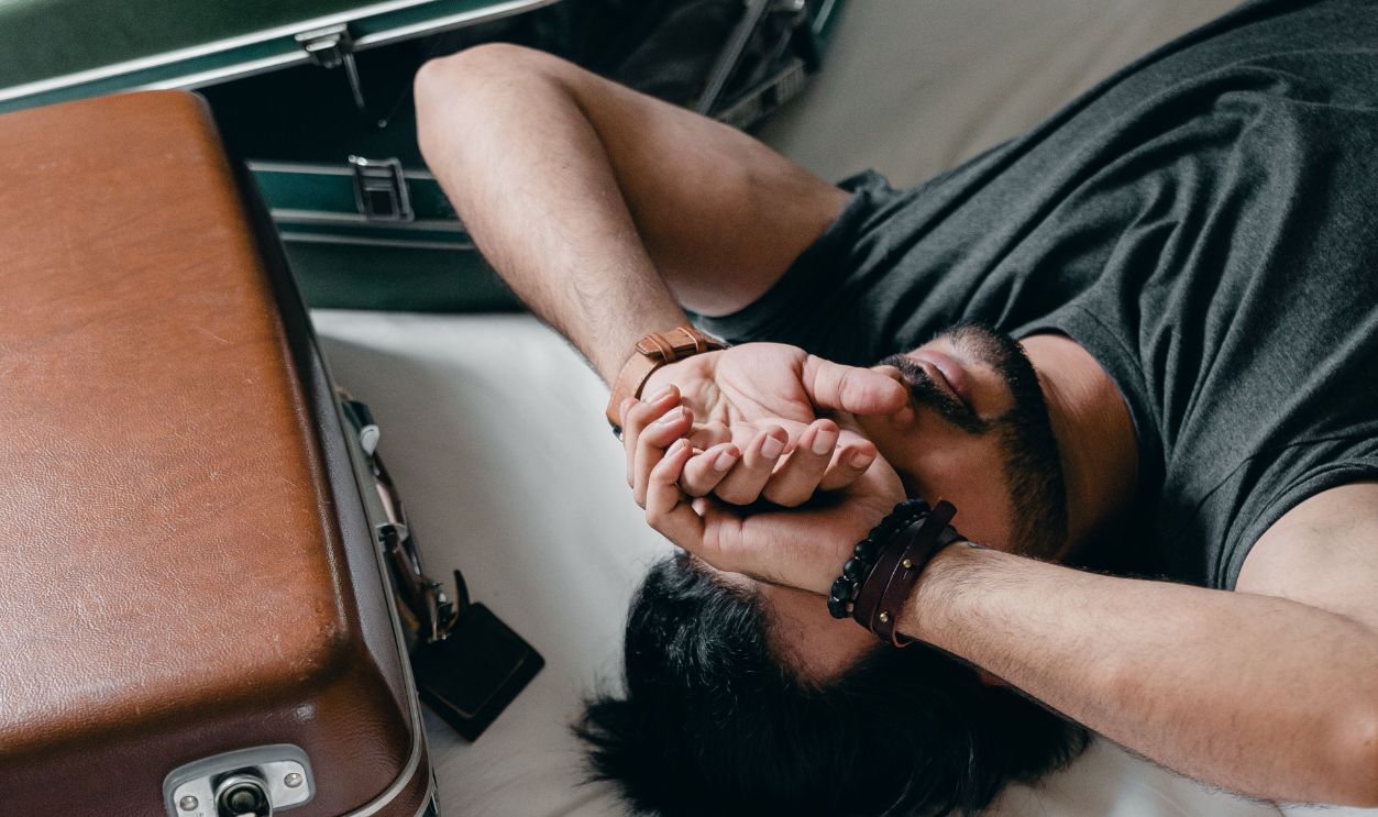 A young man rests on a bed, surrounded by luggage, reflecting a travel or moving theme