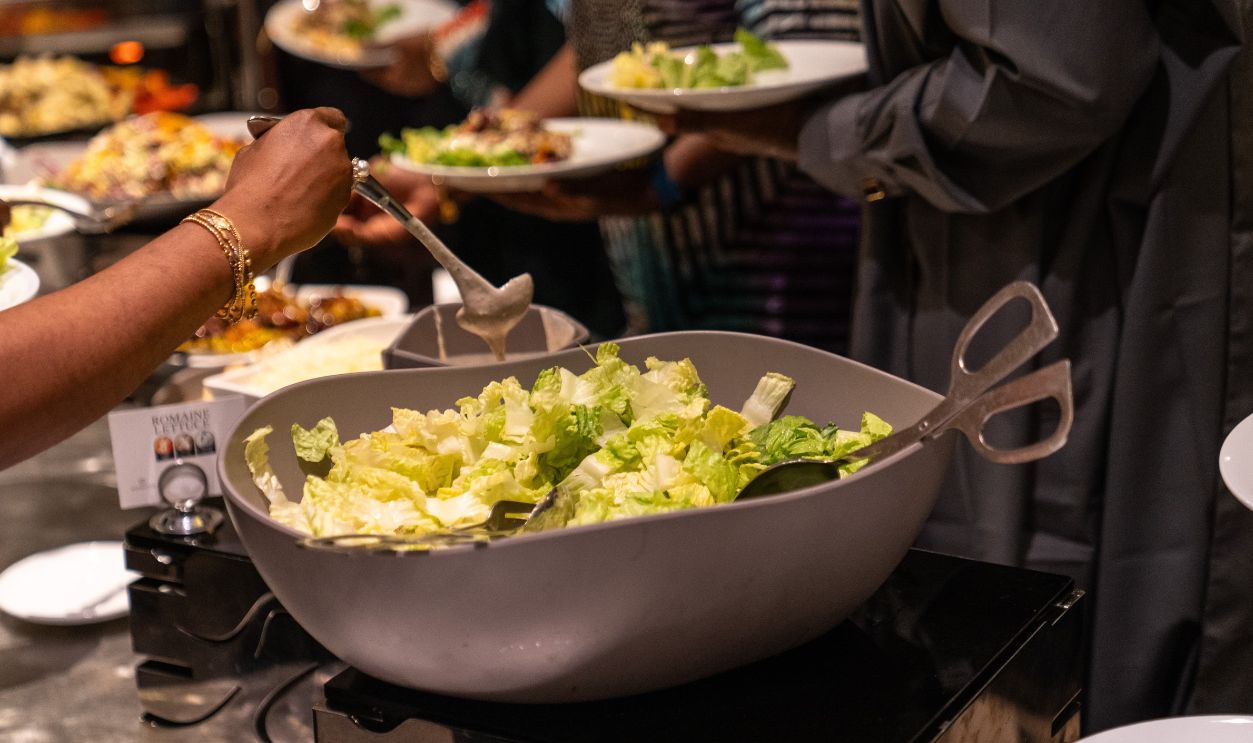A person serving green lettuce salad at a buffet during a social gathering indoors