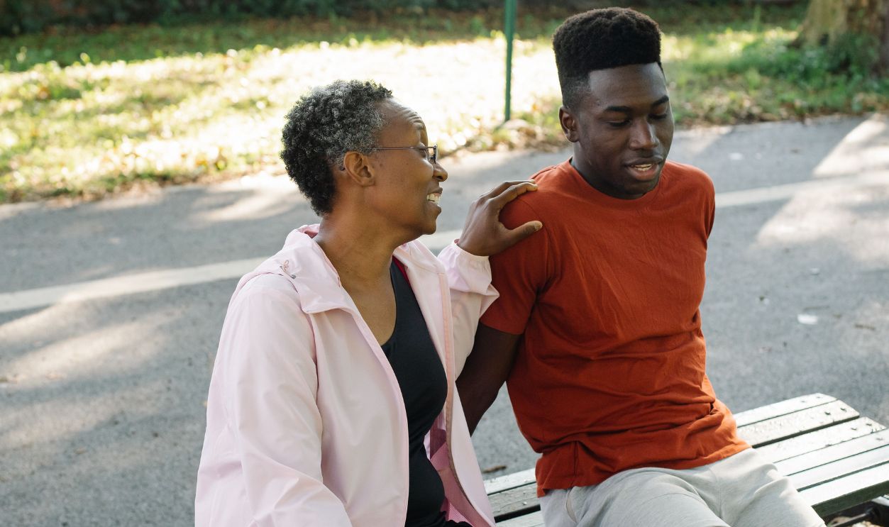 A mother and son share a moment on a park bench on a sunny day