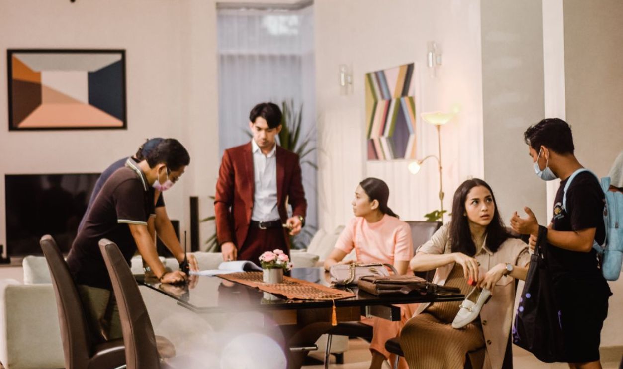 Young professionals engaging in a casual office meeting, wearing masks and discussing in a modern setting.
