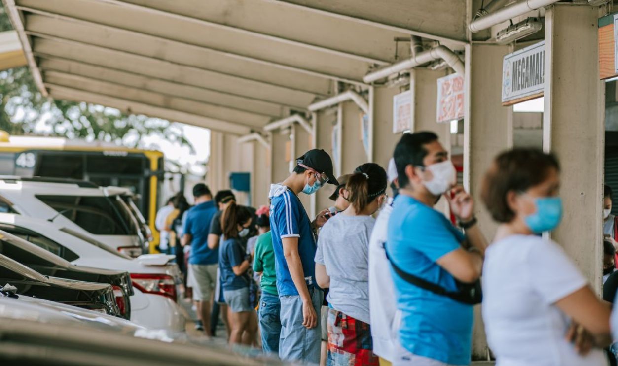 A group of people wearing face masks standing in line at an outdoor location.