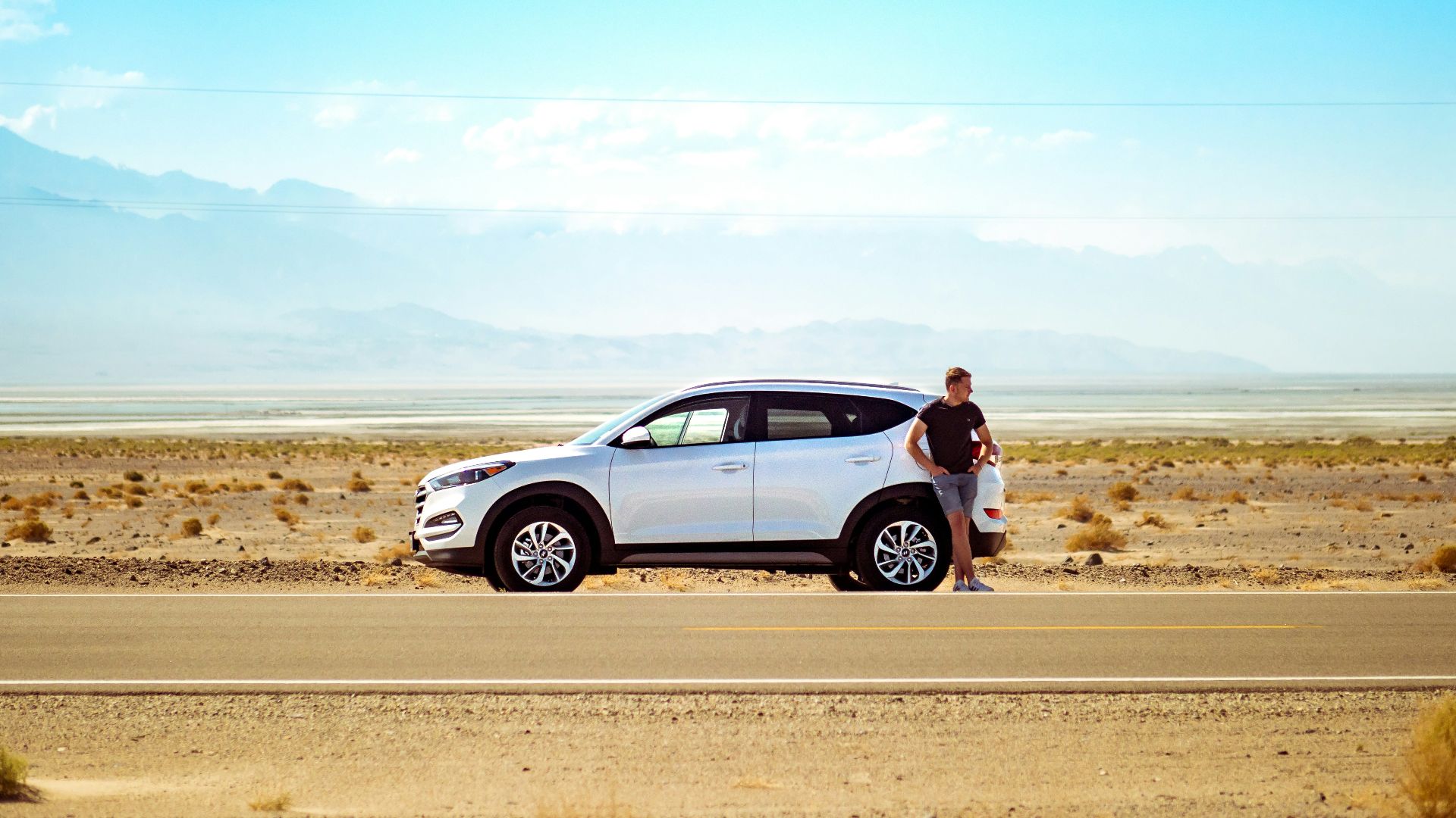 man standing beside white SUV near concrete road under blue sky at daytime