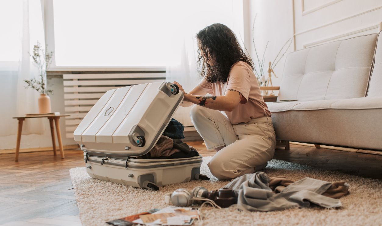 A woman packing her suitcase in a stylish living room, surrounded by clothes