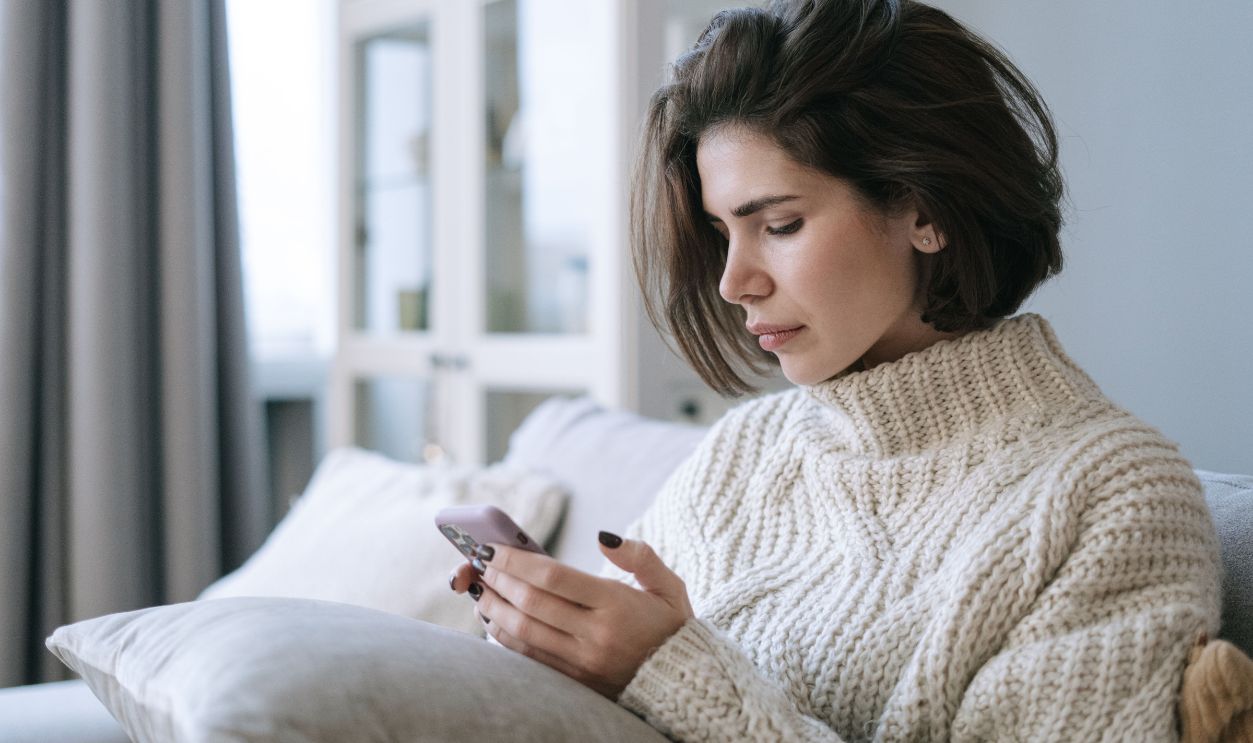 Woman in knitted sweater using smartphone on a cozy sofa