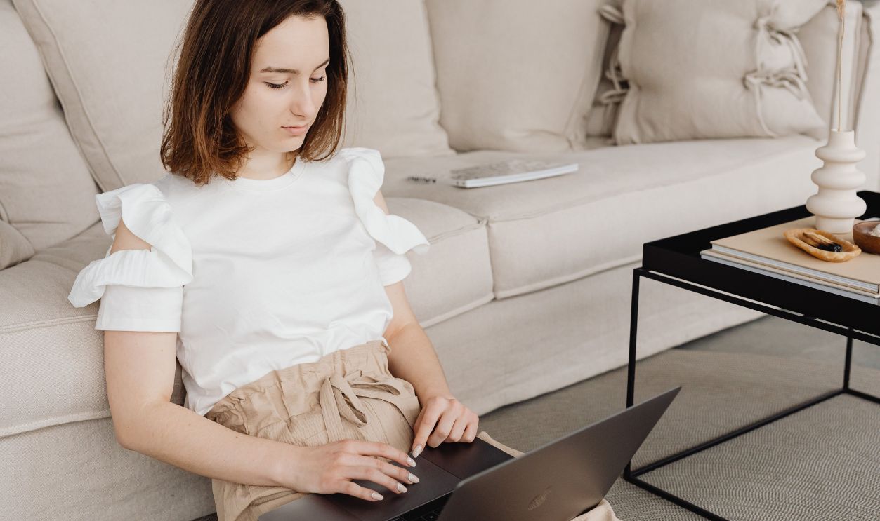 A woman sits on the floor using a laptop for remote work