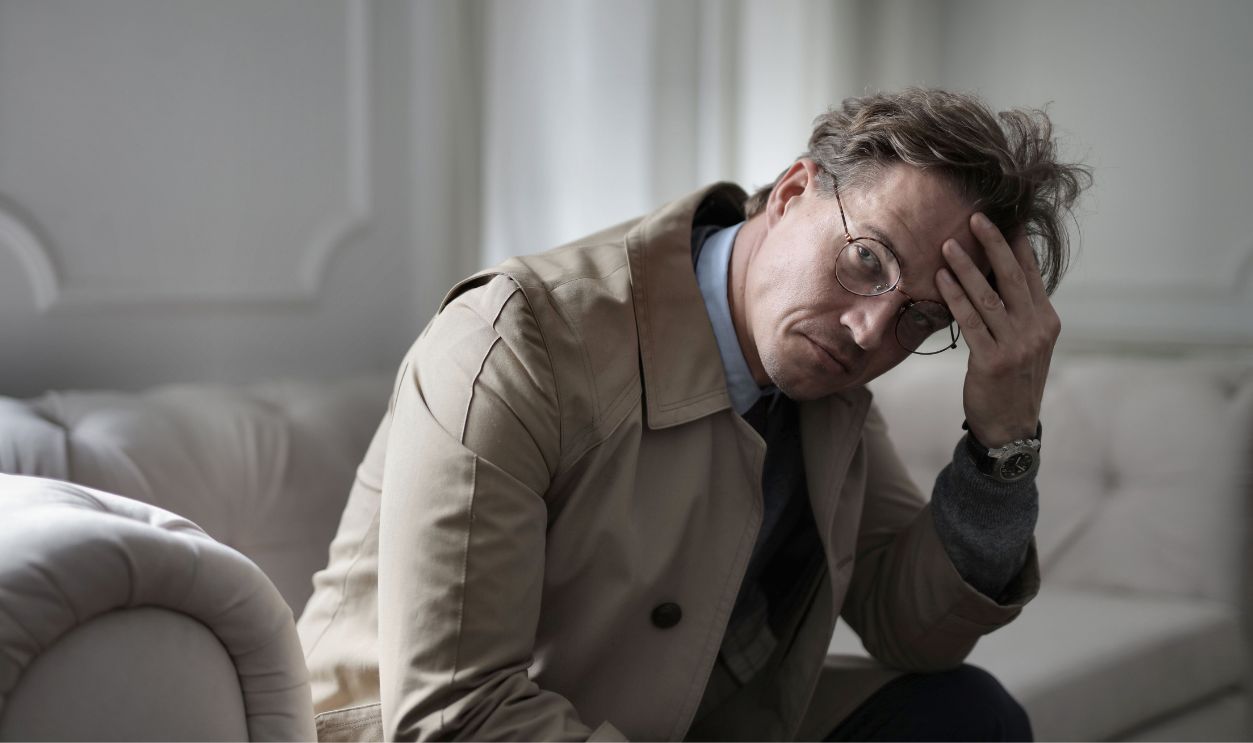 A man wearing glasses looks pensive on a sofa, conveying a mood of contemplation