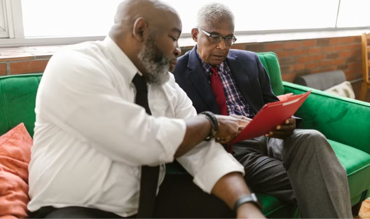 Two men discussing documents on a green sofa in a business setting
