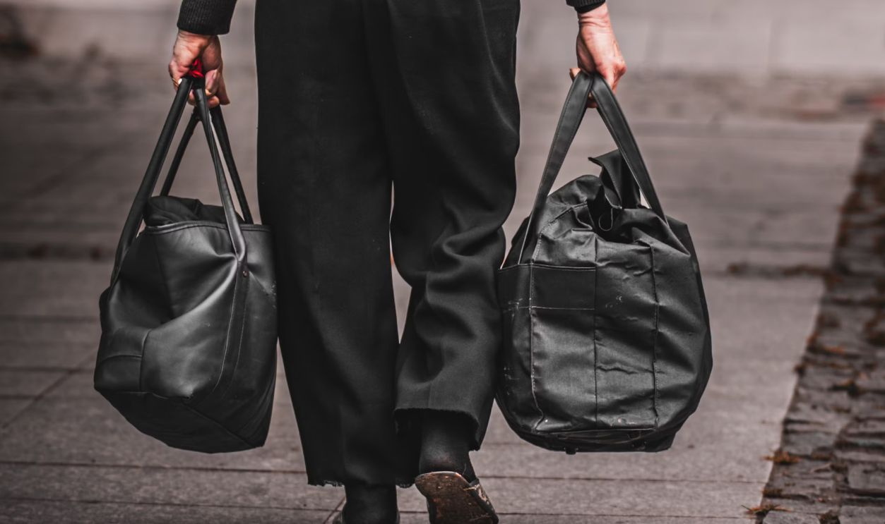 A woman dressed in black walks down a city sidewalk carrying two bags. Urban street scene