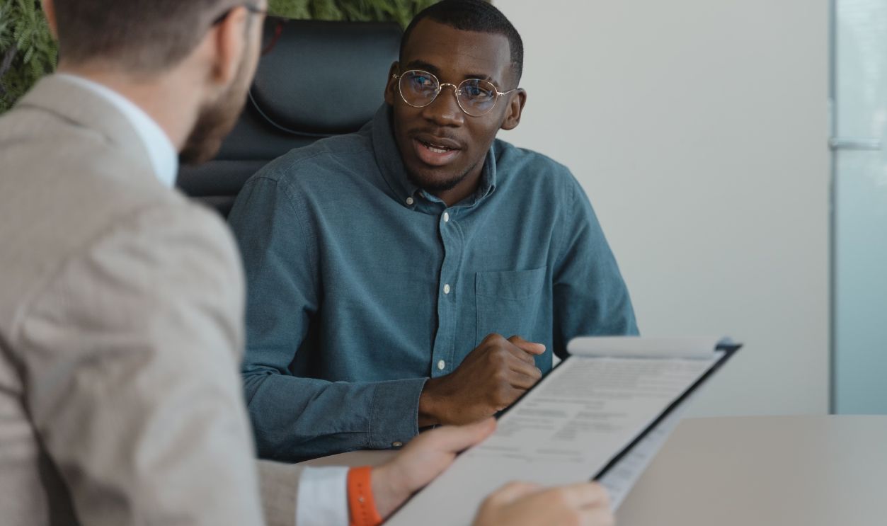 Two men engaged in a professional meeting at an office table with documents and a plant wall background