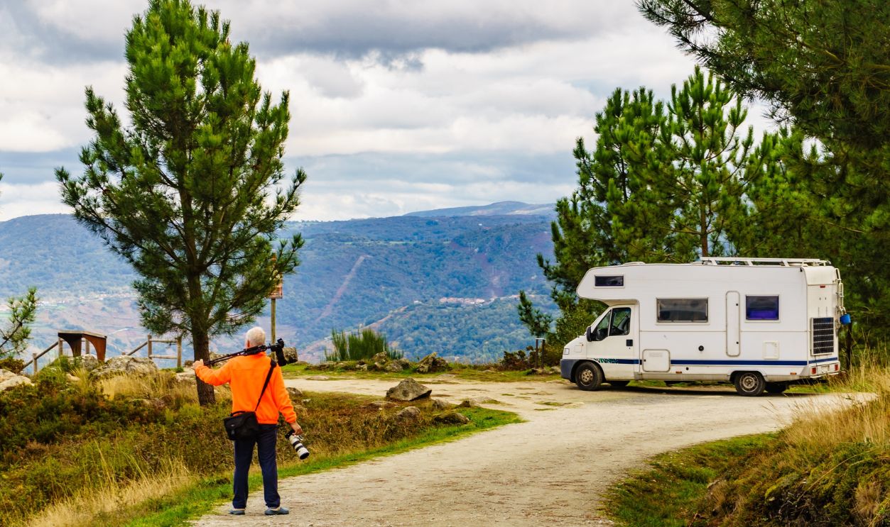 Man enjoying travel with motor home, holds camera and tripod, taking travel picture in mountain nature. Photography on vacation trip.