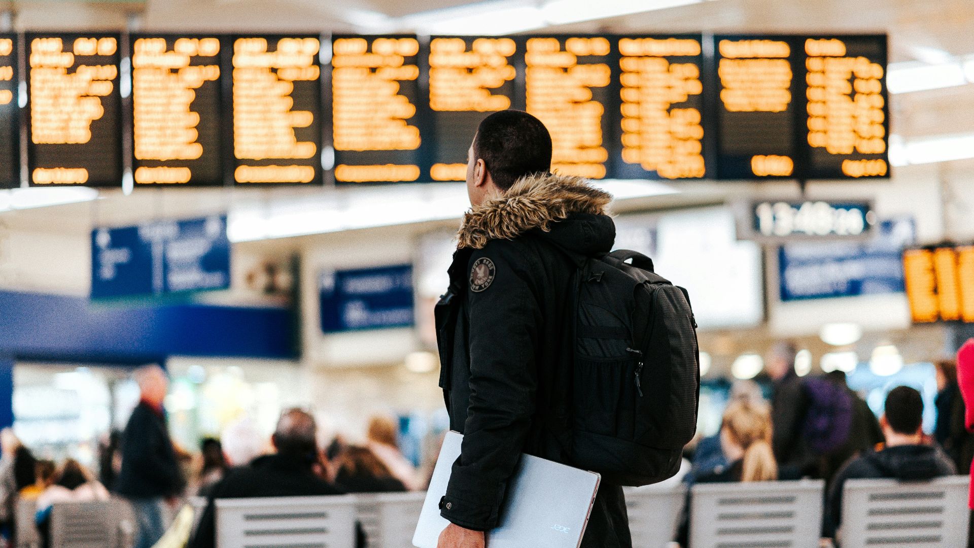 man standing inside airport looking at LED flight schedule bulletin board
