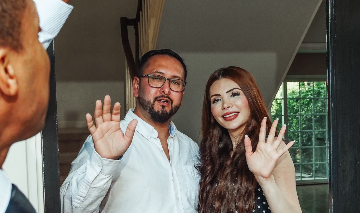Couple waving goodbye to realtor in their new home, symbolizing a successful real estate purchase