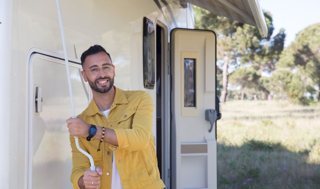 A smiling man in a yellow jacket relaxes by his camper van outdoors in Portugal