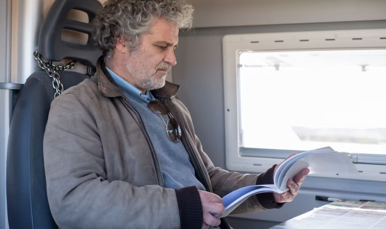 An adult man reading a book while sitting on a train in Portugal, providing a relaxed travel moment