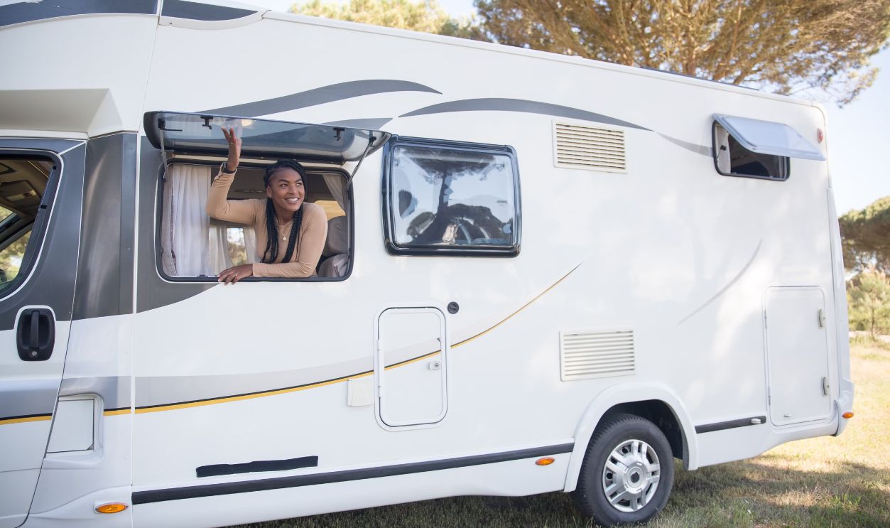 A woman smiles from a motorhome window during a sunny road trip in Portugal