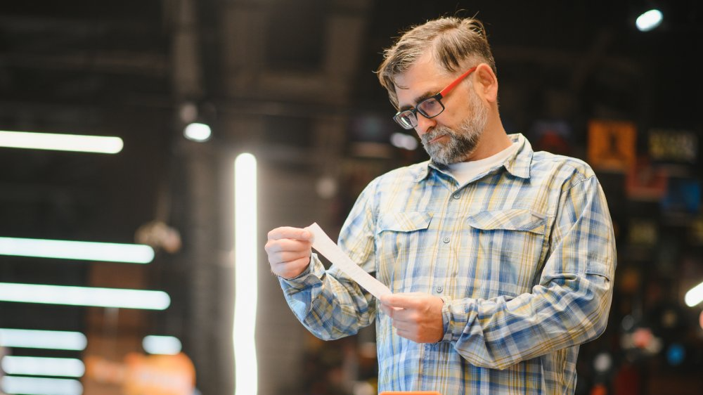 Minded man viewing receipts in supermarket and tracking prices