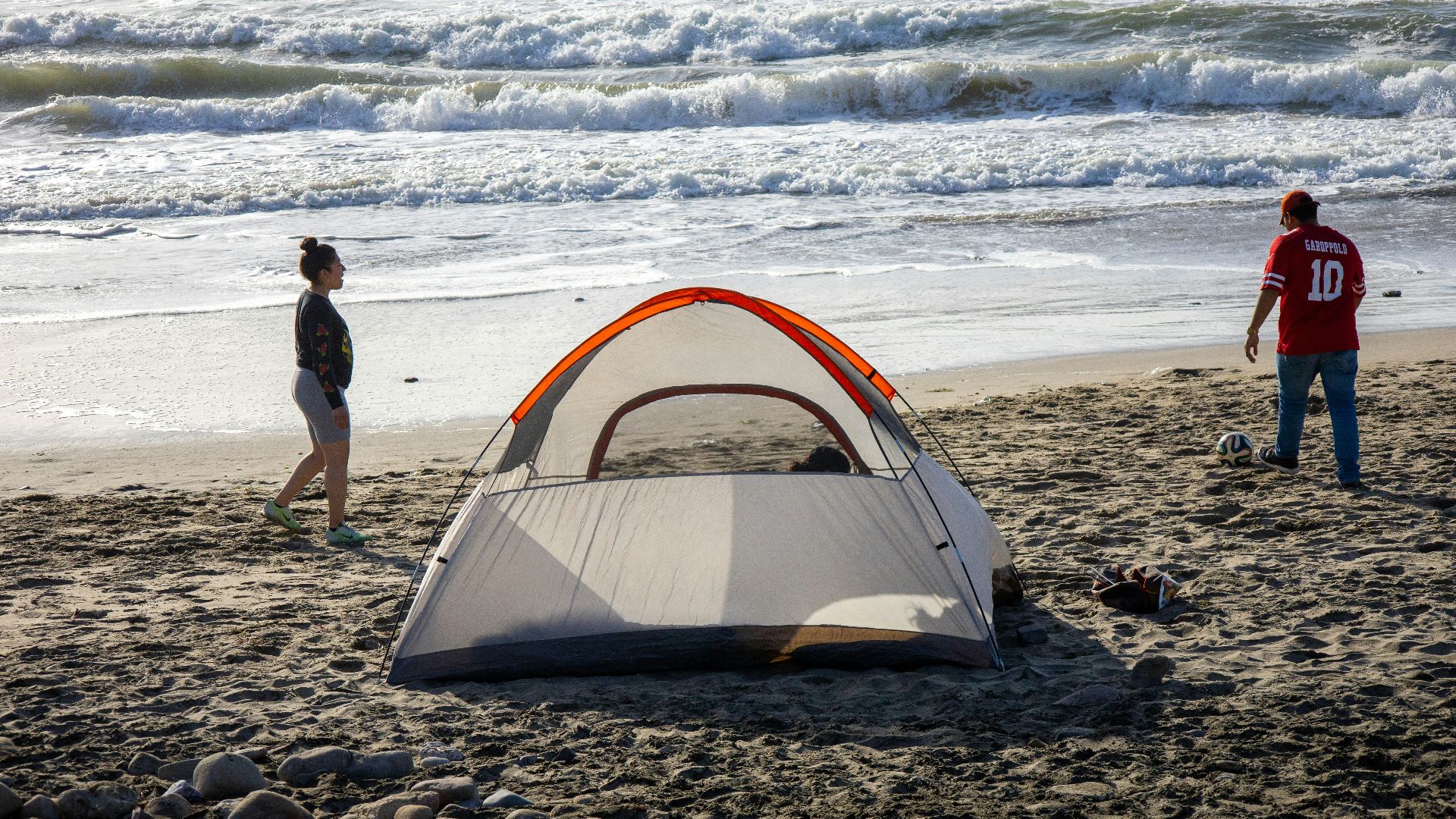 man in black t-shirt standing near orange tent on beach during daytime