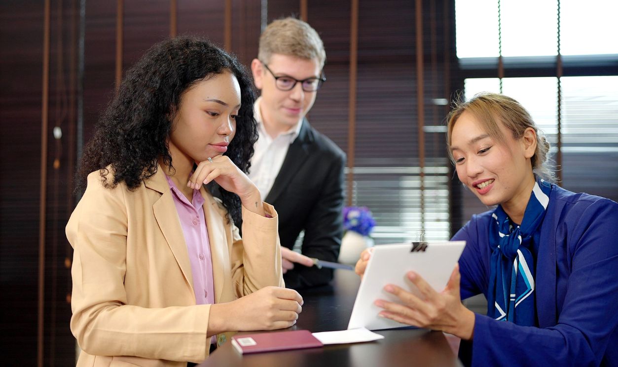Shutterstock-2310318557, Asian women hotel receptionist in uniform giving hotel information service to business men and women couple at hotel counters. Young couples on business trips check in at hotels